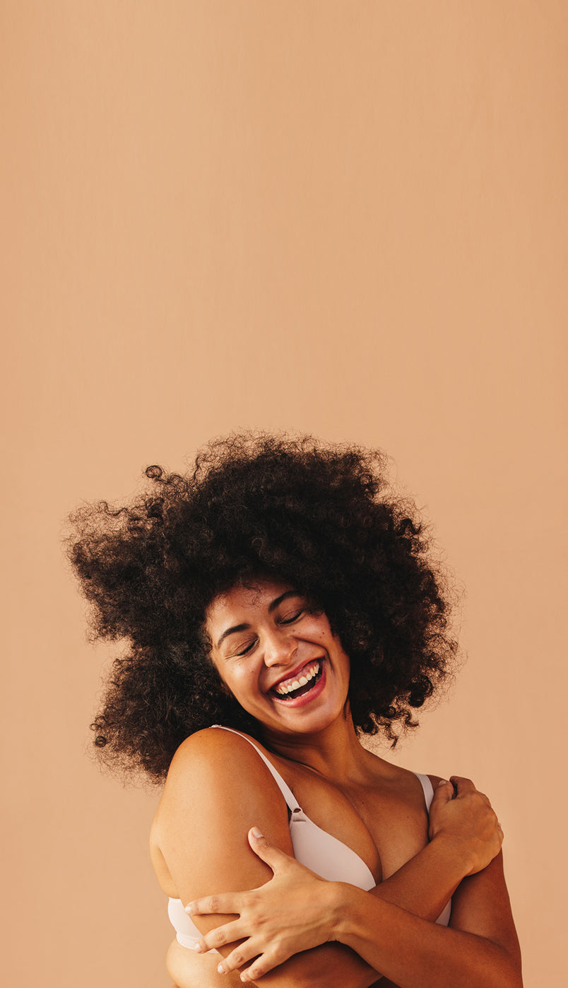 Woman with curly hair embracing herself against a beige background